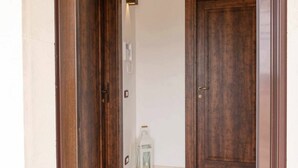 Un couloir avec deux portes en bois, une lanterne blanche et un luminaire fixé au mur.