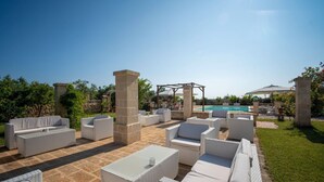 Un espace extérieur aménagé en terrasse, avec des meubles en osier, un sol en pierre et une piscine en arrière-plan.