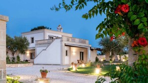 A modern two-story house with a balcony, surrounded by a well-maintained garden and outdoor seating area. - TERRA TERRA - Masseria Minunni - Suite C.Tartara (Conversano)