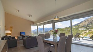 A modern living room with a dining area, large windows offering a mountain view, and a flat-screen TV on a stand. - La Estrella by Interhome (Altea)