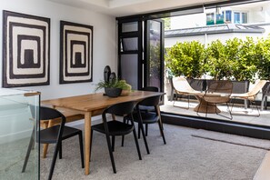 A modern dining area with a wooden table, black chairs, and a glass partition. There are two framed artworks on the wall and a potted plant on the table. - Designer Seaview Chic accommodation for the discerning traveler (Mount Maunganui)