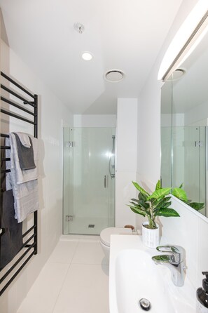 A modern bathroom with a glass shower enclosure, a white sink, and a potted plant. - Designer Seaview Chic accommodation for the discerning traveler (Mount Maunganui)