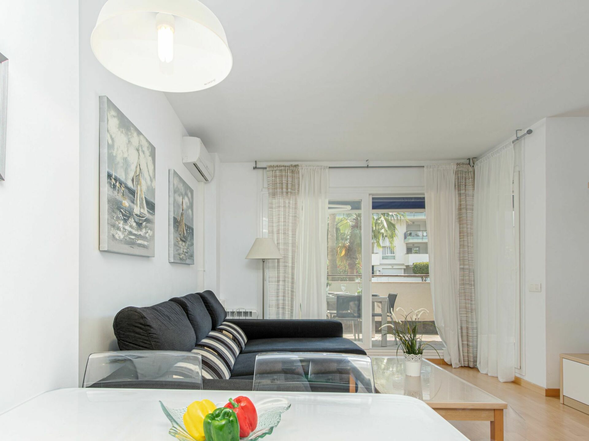 Una sala moderna con un sofá, una mesa de comedor con frutero y vistas a un balcón con planta.
