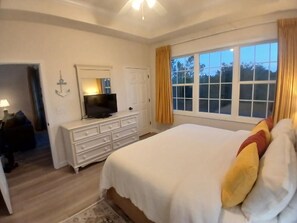 A bedroom with a large bed, a dresser, a television, and a window with curtains.