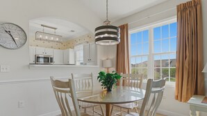 A dining area with a round table, chairs, a clock, and a view of the outdoors. - 🏝 Barefoot Landings in N Myrtle Beach-2 Resort Pools/ Golf/  8 Mins to Beach 🏝 (North Myrtle Beach)