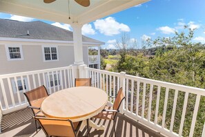A covered patio with a round table and chairs, white railings, and a view of a house and landscape.
