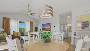 A spacious living room with a round glass table, white chairs, a ceiling fan, and a large window with curtains. - 🏝 Barefoot Landings in N Myrtle Beach-2 Resort Pools/ Golf/  8 Mins to Beach 🏝 (North Myrtle Beach)
