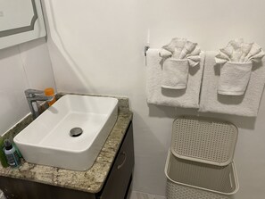 A bathroom with a white sink, a towel rack with two towels, and a laundry basket. - Eddy’s Beachfront Apartment  (Ocho Rios)