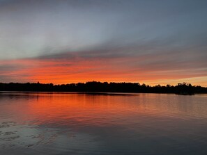 Un llac tranquil al capvespre amb la silueta d'arbres i un vaixell a l'aigua.