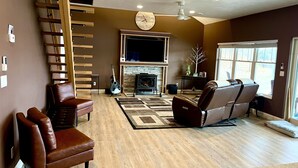 A living room with a fireplace, a ceiling fan, and a large window. - Peaceful Private Waterfront Home (Redwood)