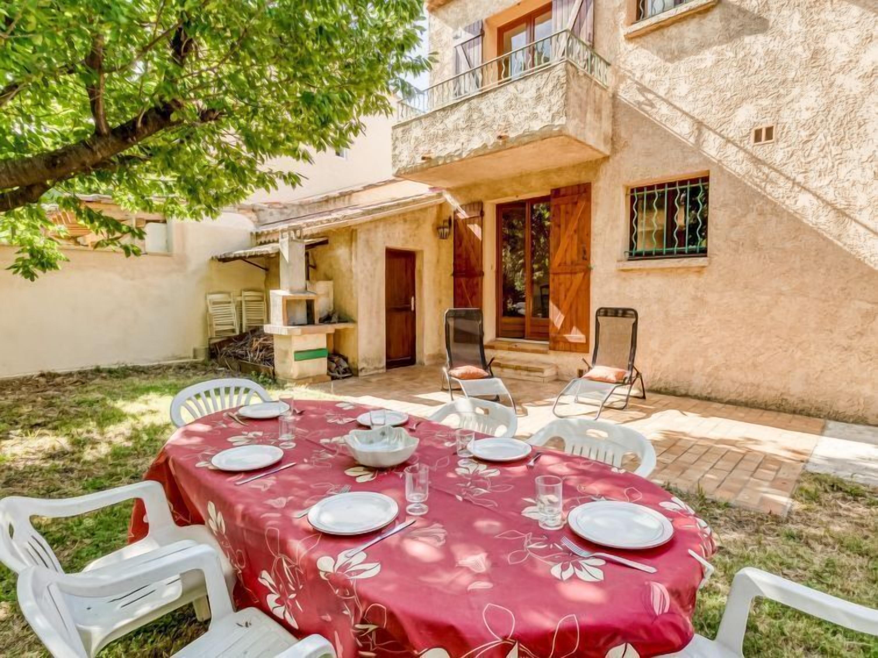 A dining area with a table set for four, surrounded by white chairs, in a courtyard with a building in the background.