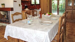 A dining room with a table set for four, wooden chairs, a pitcher, a bowl of fruit, and a view of the kitchen and outdoors. - L'ensoleillade by Interhome (Saint Cyr sur mer Les Lecques)