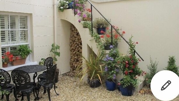 A small outdoor seating area with a table and chairs, surrounded by potted plants and a staircase with hanging flower baskets. - Private luxury apartment near Belfast with garage (Holywood)