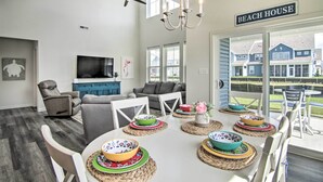 Un salon spacieux comprenant un coin repas, un téléviseur et une pancarte indiquant « MAISON DE PLAGE ».