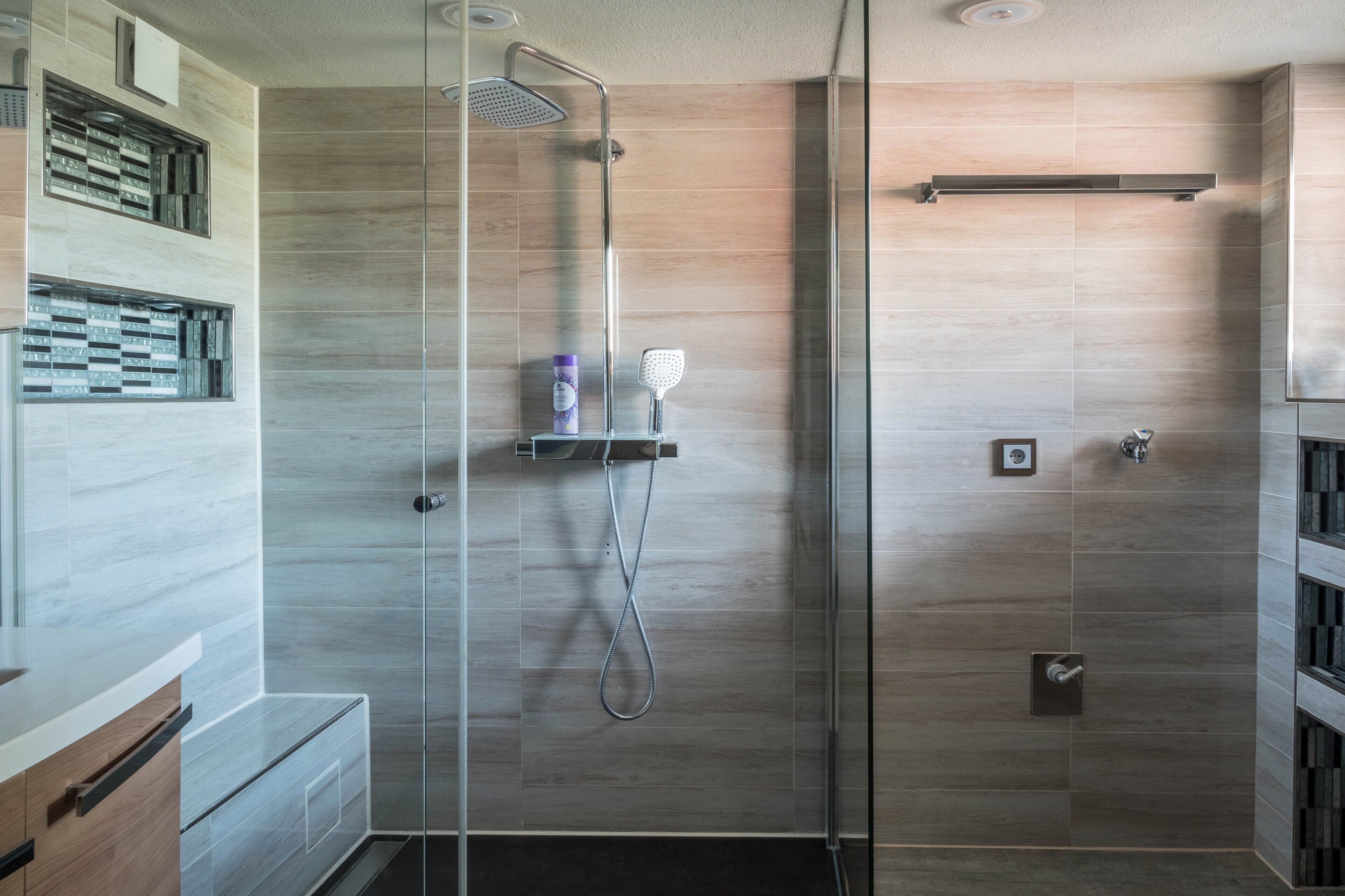 Une salle de bain moderne avec une douche à parois de verre, un meuble-lavabo en bois et un mur recouvert de carreaux.