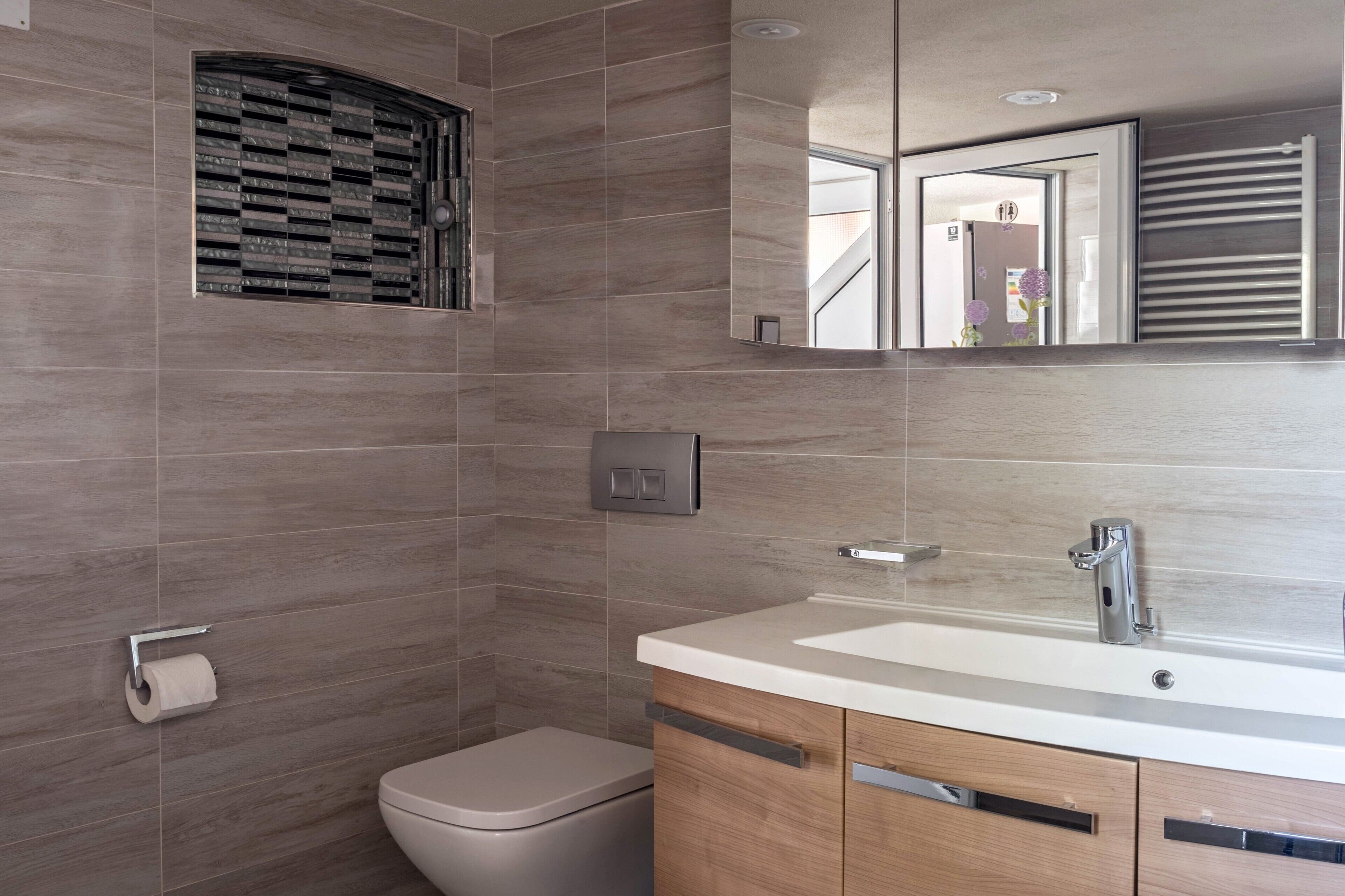 A modern bathroom with a toilet, a sink, a mirror, and a shower with a window.