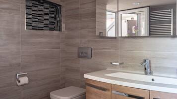 A modern bathroom with a toilet, a sink, a mirror, and a shower with a window.