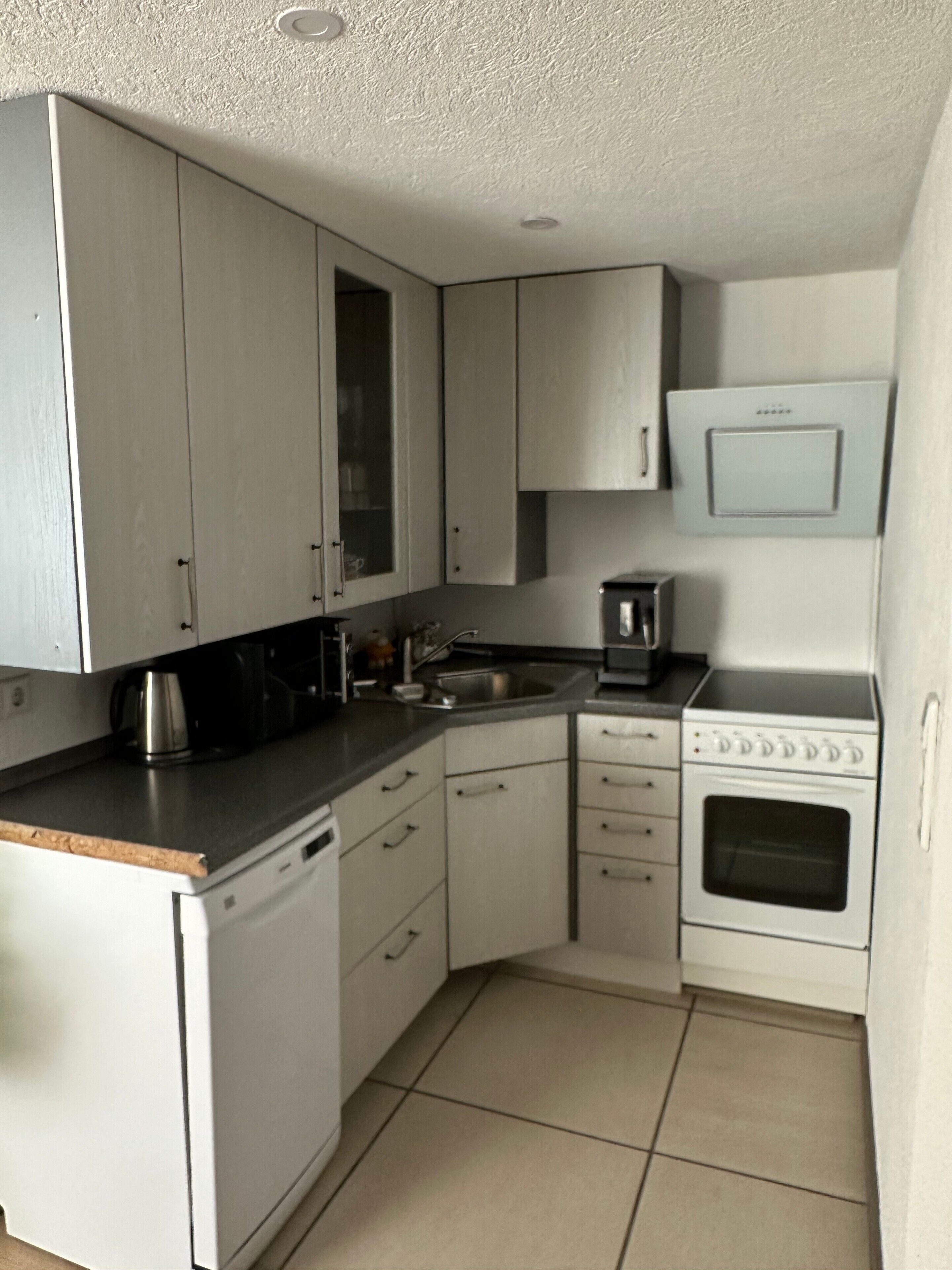 Een kleine keuken met witte kastjes, een magnetron, een koffiezetapparaat en een vaatwasser.