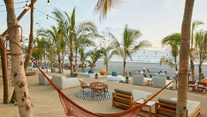 En avslappnad lounge vid stranden med hängmattor, sittplatser och en mönstrad matta.