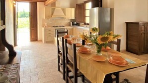 Uma área de refeições com uma mesa posta para quatro pessoas, cadeiras de madeira e um vaso com girassóis.