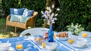 En morgenmadsopsætning med et bord ude, inklusiv skåle, en vase med blomster, croissanter og et glas appelsinjuice.