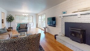 Un salon avec une cheminée, un canapé, un fauteuil à motifs et un téléviseur fixé au mur.