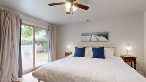 Une chambre avec un grand lit, un ventilateur de plafond, un tableau et une vue sur l’extérieur.