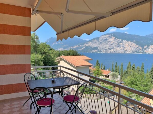 A balcony with a table and chairs, overlooking a mountainous landscape and a body of water.
