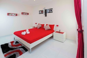 A modern bedroom with a red bedspread, white nightstands, and a red curtain.