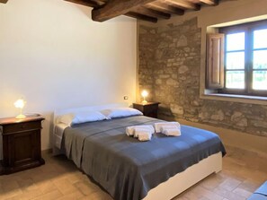 Quarto com cama, duas mesas de cabeceira, parede de pedra e uma janela.