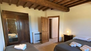 Habitación de hotel con dos camas, puertas de madera, una mesita con lámpara y vistas a un muro de piedra reflejado en un espejo.