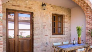 Un patio exterior rústico con una mesa y sillas de madera, una planta en maceta y una botella de vino.