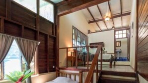 Quarto com cama, escada de madeira e vista para outro cômodo.