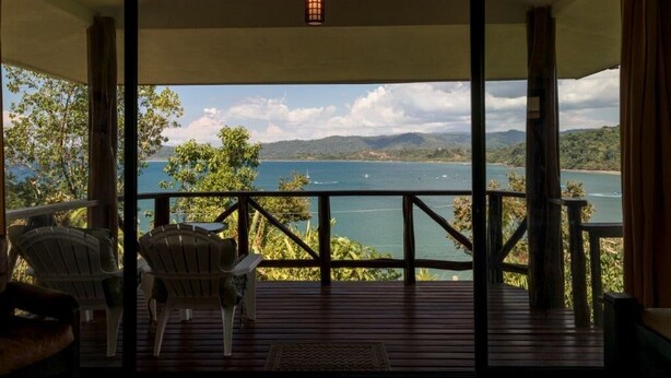Um deck de madeira com cadeiras, com vista para um lago e montanhas.