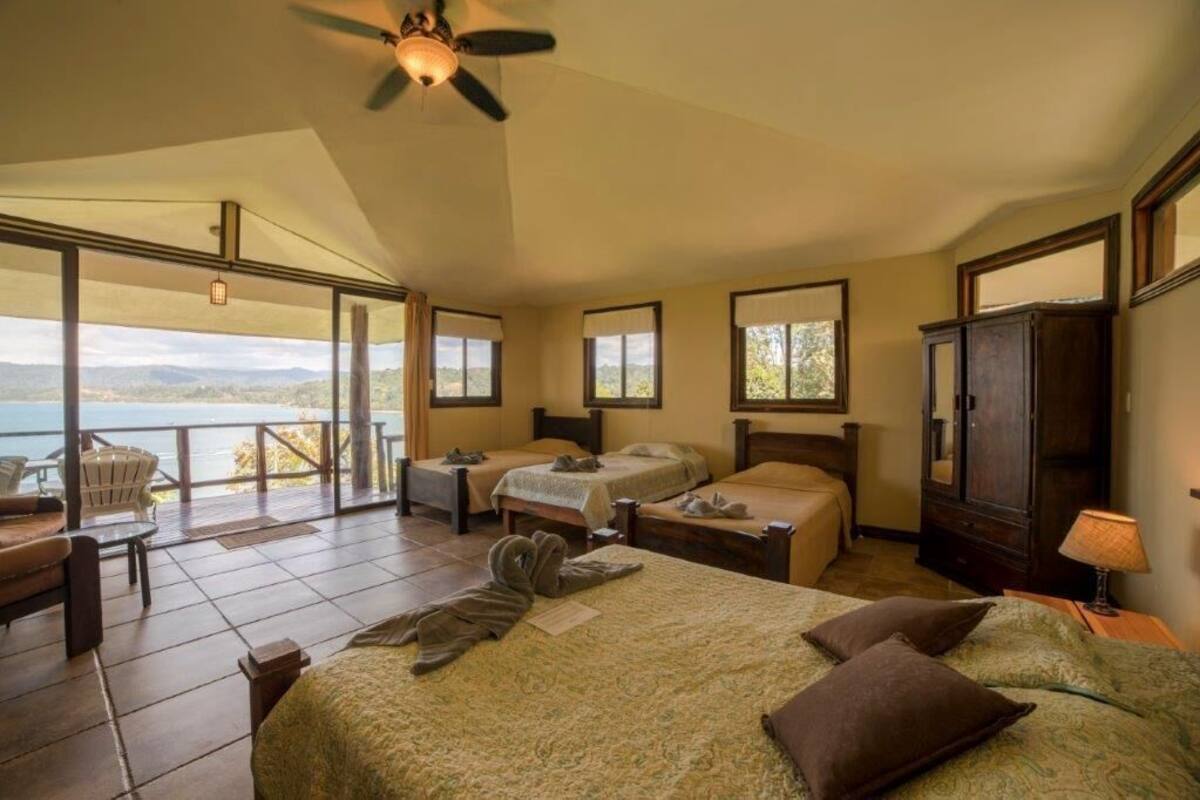 A bedroom with a large bed, two smaller beds, a wardrobe, and a balcony with a view.