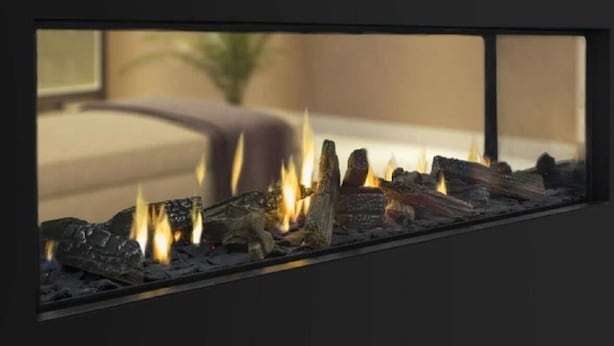 A fireplace with burning logs and a sofa in the background. - Luxury Accommodation - Harris (Montville)