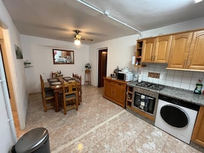 A kitchen with wooden cabinets, a gas stove, a microwave, and a dining area with a table and chairs. - Holiday Home 'Casa Margarita' with Mountain View, Wi-Fi and Air Conditioning (Algarinejo)