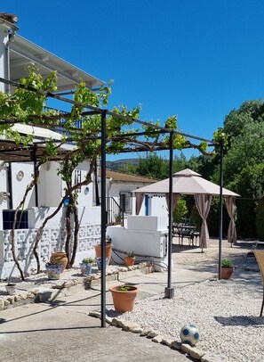 A white building with a pergola covered in green vines, outdoor seating, and potted plants. - Holiday Home 'Casa Margarita' with Mountain View, Wi-Fi and Air Conditioning (Algarinejo)