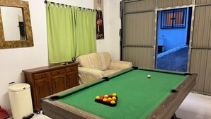 A pool table with balls, a sofa, a cabinet, a mirror, and a window with curtains.