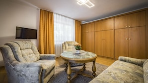 A living room with two armchairs, a coffee table with a vase of flowers, a television on the wall, and wooden cabinets. - Apartment Sophia, 60sqm, 1 bedroom, balcony with mountain view (Bad Reichenhall)