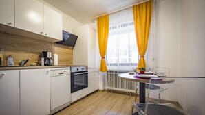 A modern kitchen with white cabinets, a dishwasher, an oven, and a window with yellow curtains. - Apartment Sophia, 60sqm, 1 bedroom, balcony with mountain view (Bad Reichenhall)