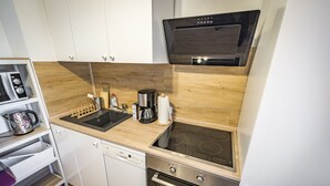 A compact kitchen with white cabinets, a dishwasher, an oven, a stovetop, and a coffee maker. - Apartment Sophia, 60sqm, 1 bedroom, balcony with mountain view (Bad Reichenhall)