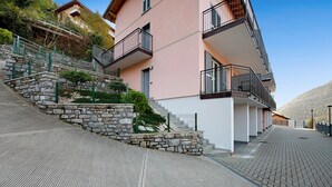 Ein mehrstöckiges Gebäude mit einer Steinstufenanlage, die zu einem Balkon führt, einem gepflasterten Weg und blauem Himmel.