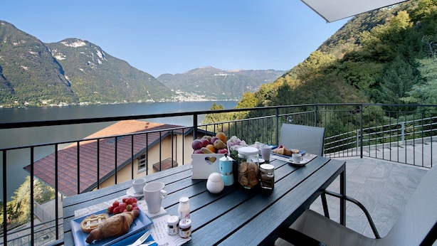 Ein Balkon mit einem Frühstückstisch, mit Blick auf einen See und Berge.