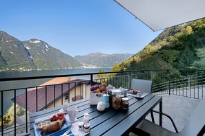 Un balcon avec une table préparée pour le petit-déjeuner, offrant une vue sur un lac et des montagnes.