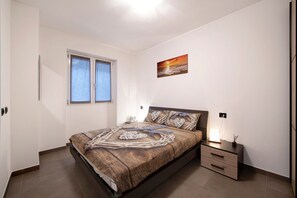 Un dormitorio con una cama, una mesita de noche, una ventana y una obra de arte colgada en la pared.