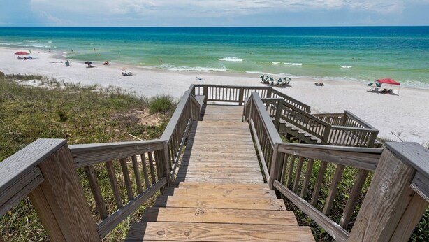 Una escalera de madera que lleva a una playa de arena blanca y agua turquesa cristalina.