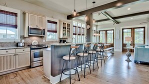 A spacious kitchen with a central island, bar stools, and a dining area with a blue sofa. - Beach Home with Gulf Views! Steps to Heated Community Pool Minutes to 30A's newest beach access! (Santa Rosa Beach)