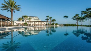 A resort with a clear infinity pool, palm trees, and a building with a white facade. - Beach Home with Gulf Views! Steps to Heated Community Pool Minutes to 30A's newest beach access! (Santa Rosa Beach)