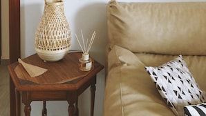 Una habitación con una mesita de madera, un farol tejido, un atrapasueños y un cojín estampado sobre un sofá color beige.